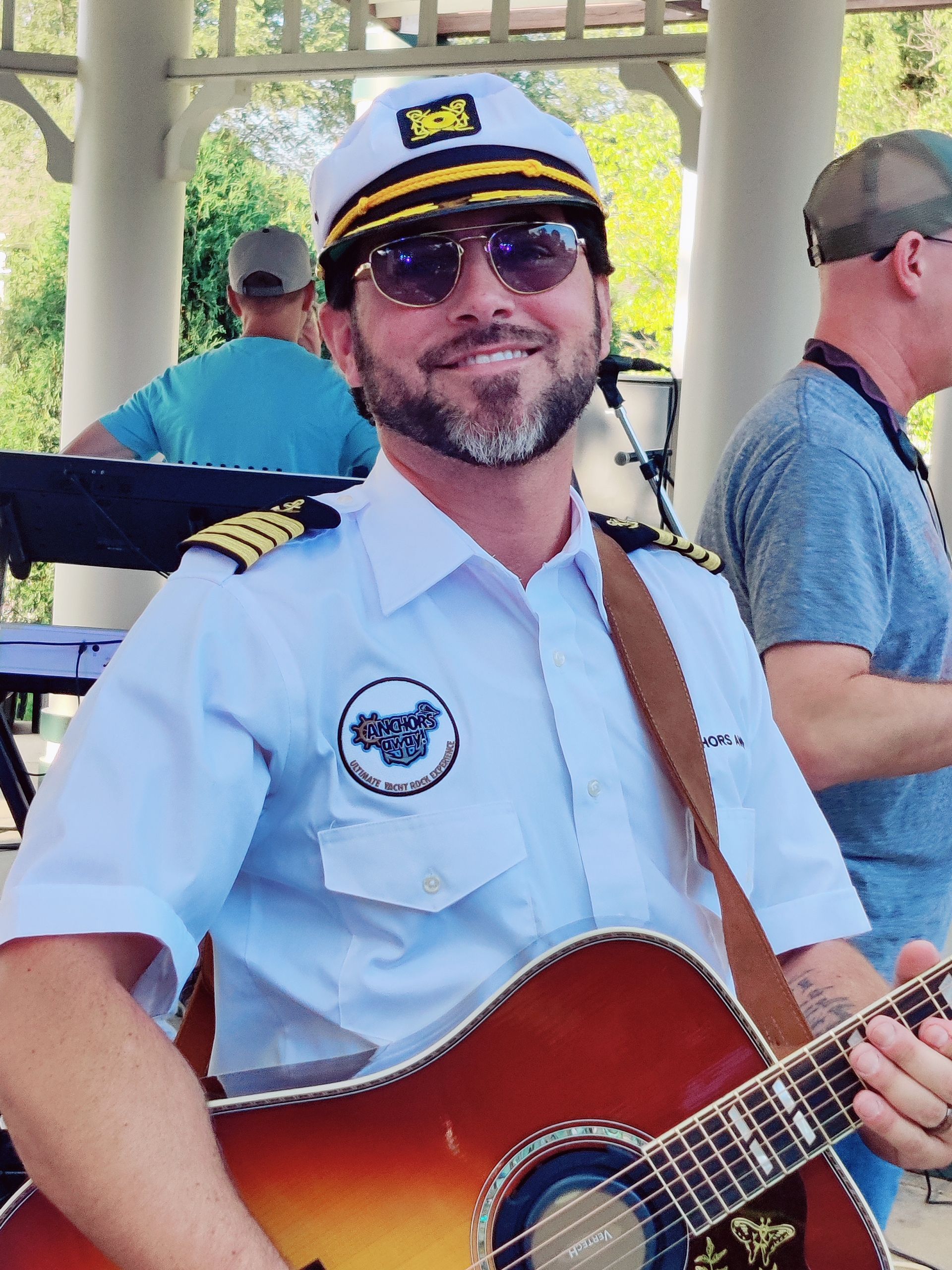 A man in a captain 's hat is holding a guitar
