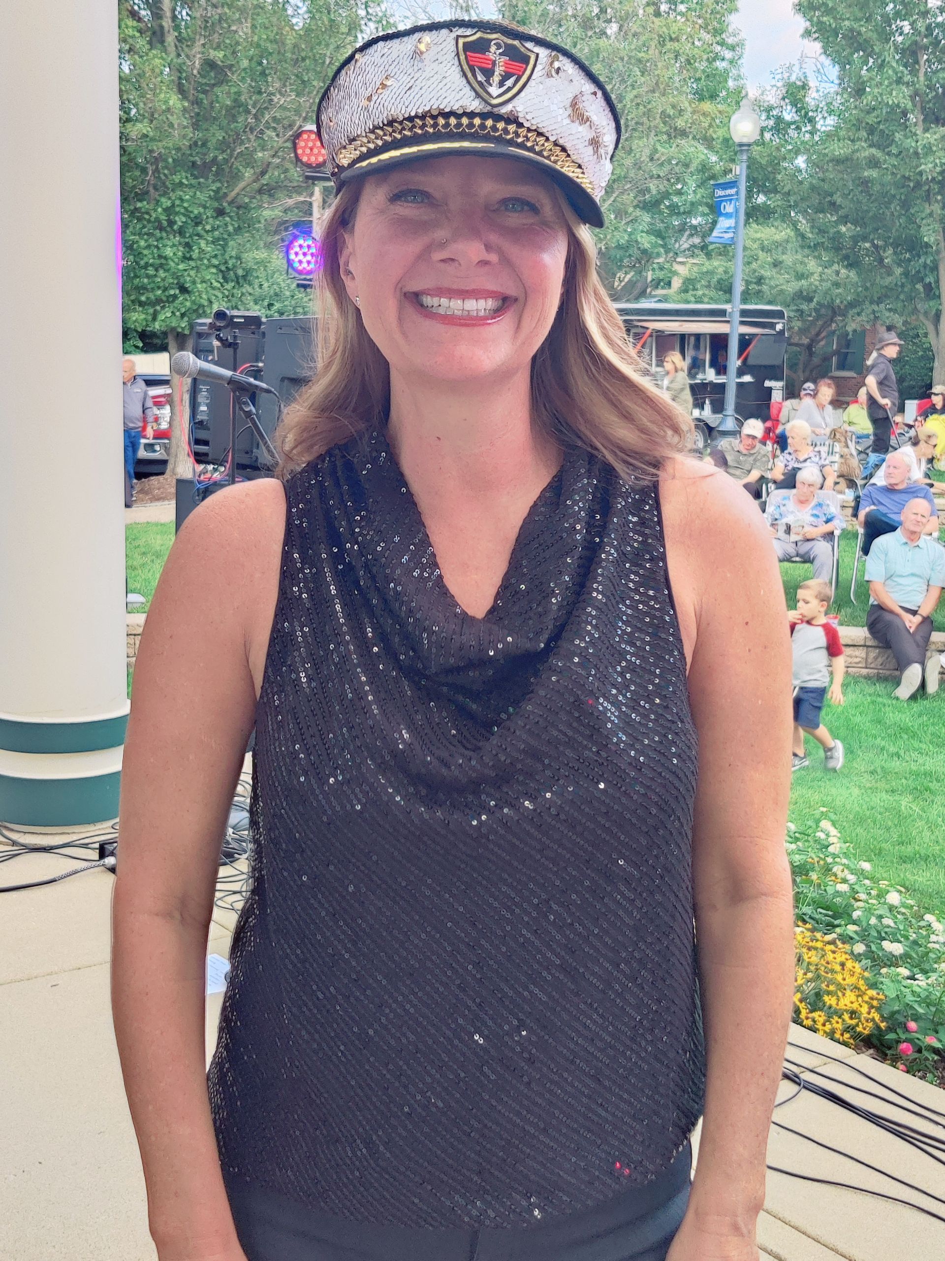 A woman wearing a hat and a sequined top is smiling