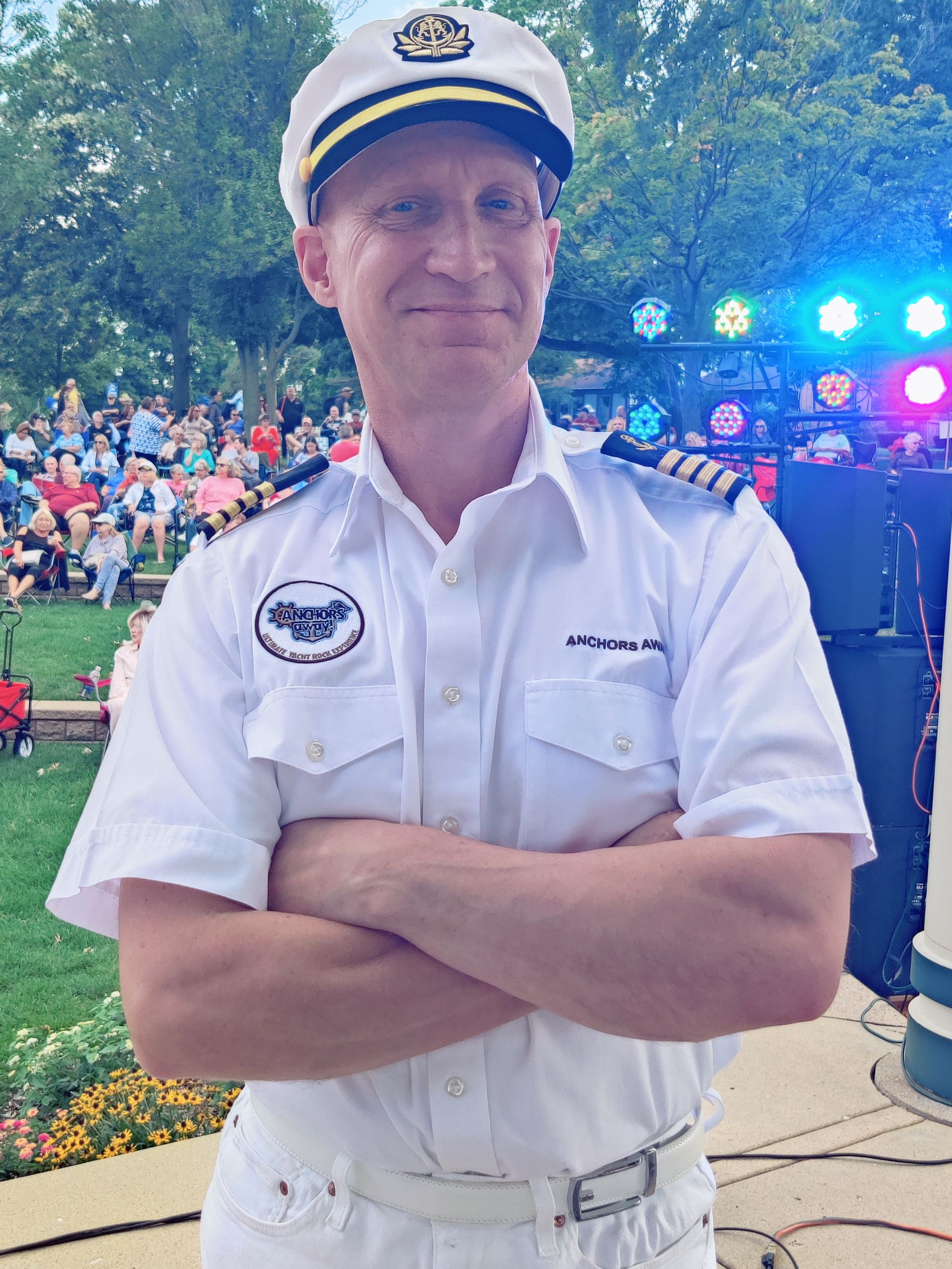 A man in a captain 's uniform is standing with his arms crossed in front of a crowd.