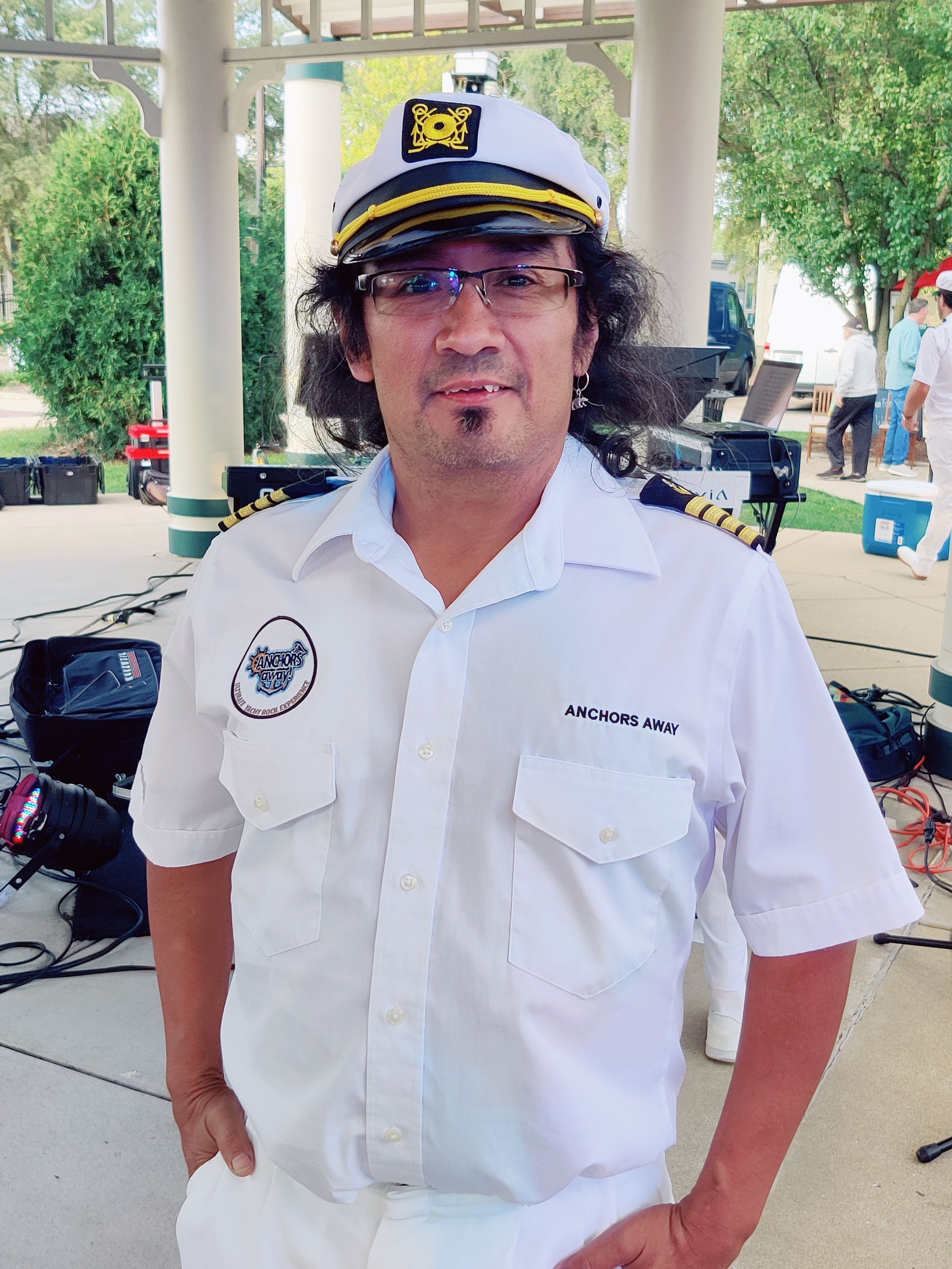 A man wearing a captain 's hat and glasses stands with his hands in his pockets