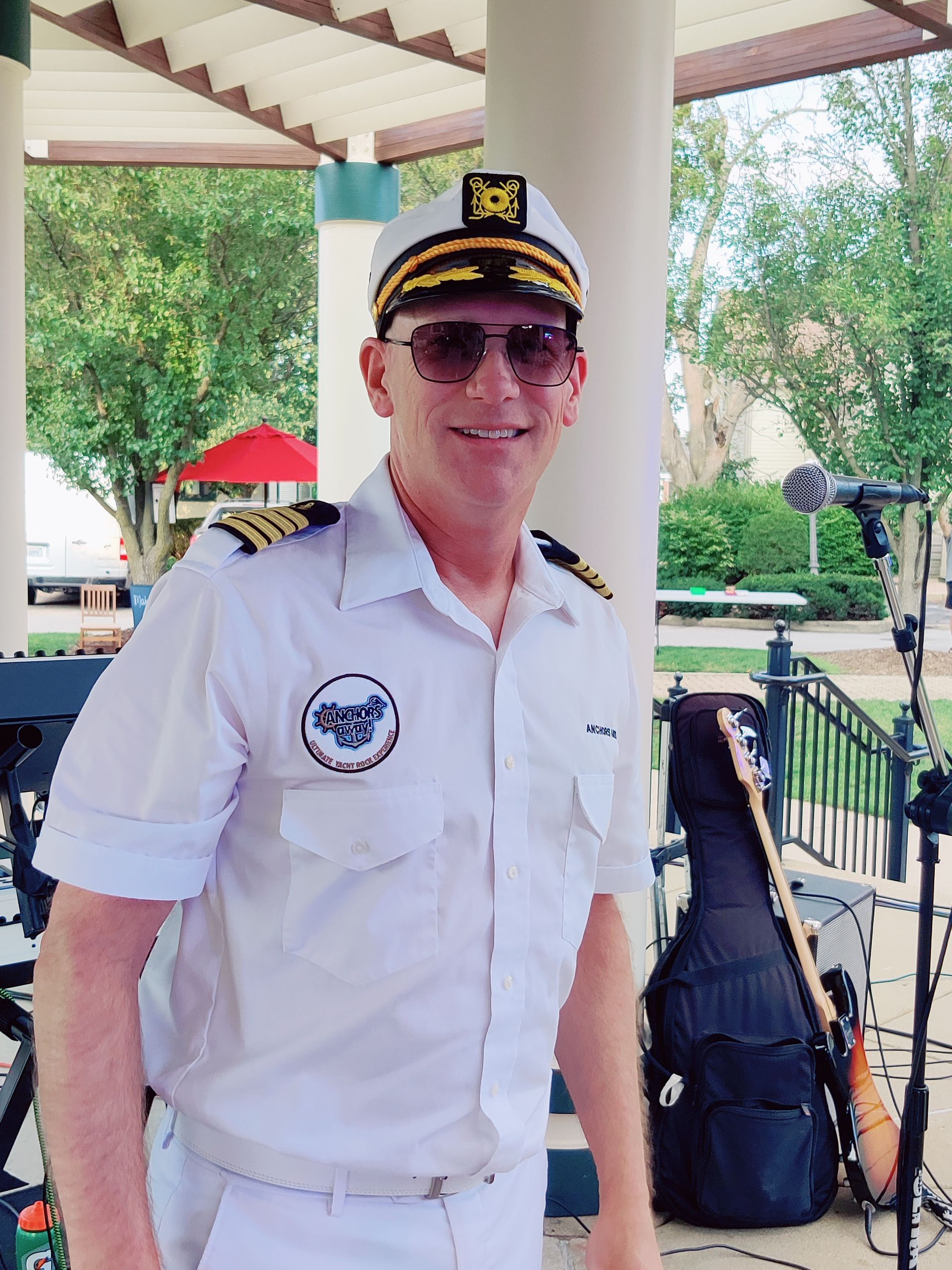 A man in a captain 's uniform stands in front of a guitar case