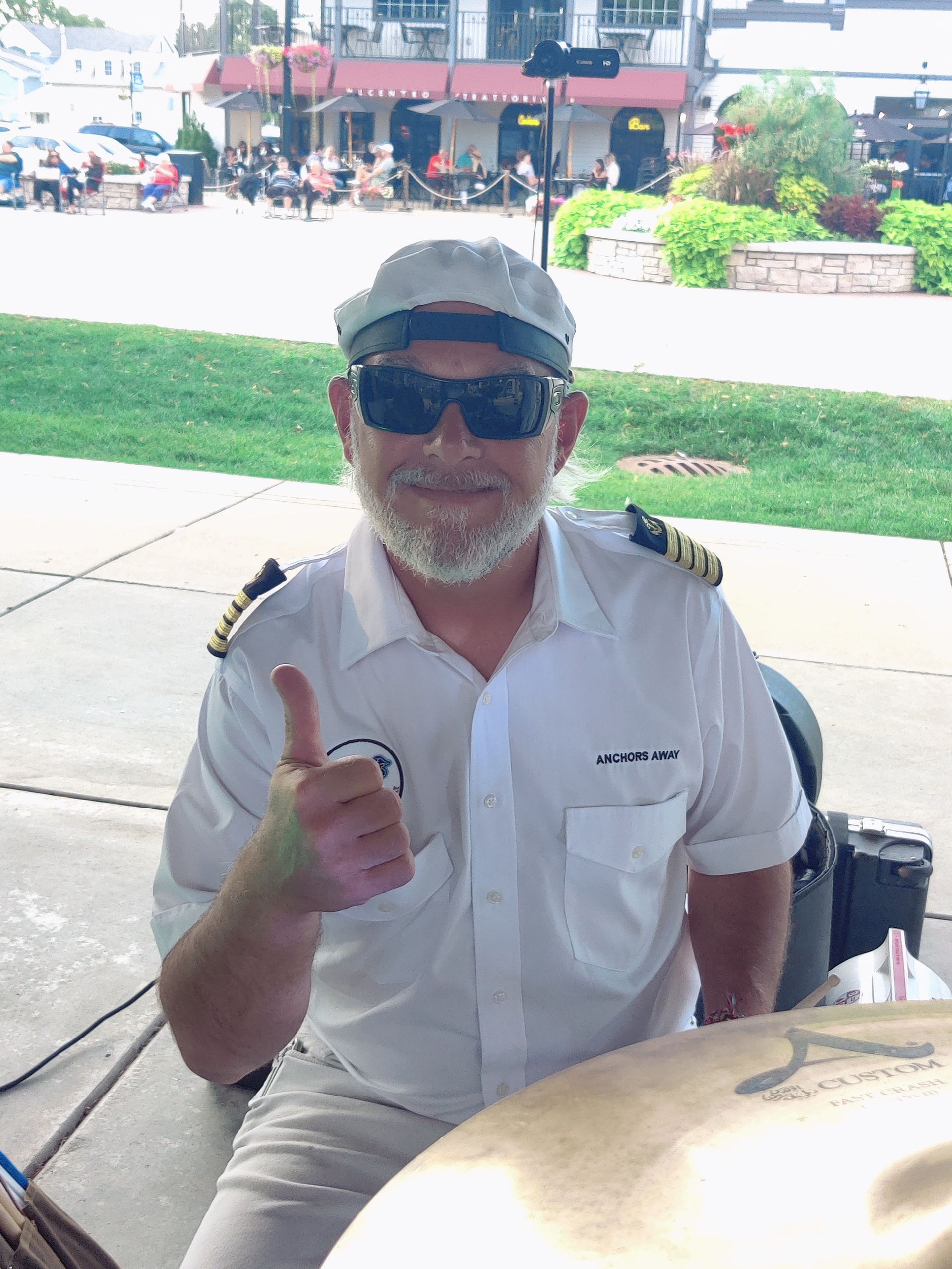 A man in a white shirt and hat is giving a thumbs up