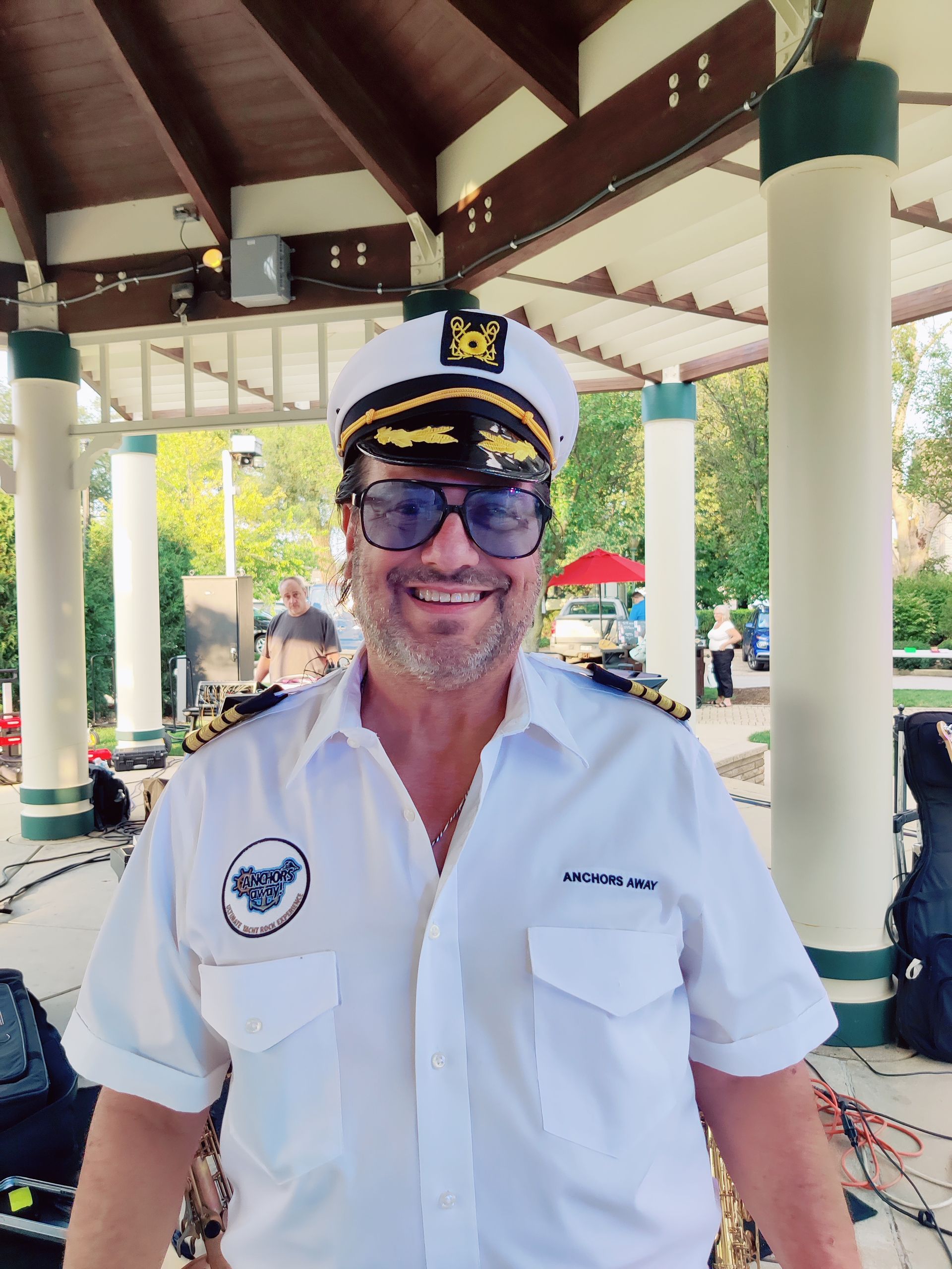 A man wearing a captain 's hat and sunglasses is smiling for the camera.