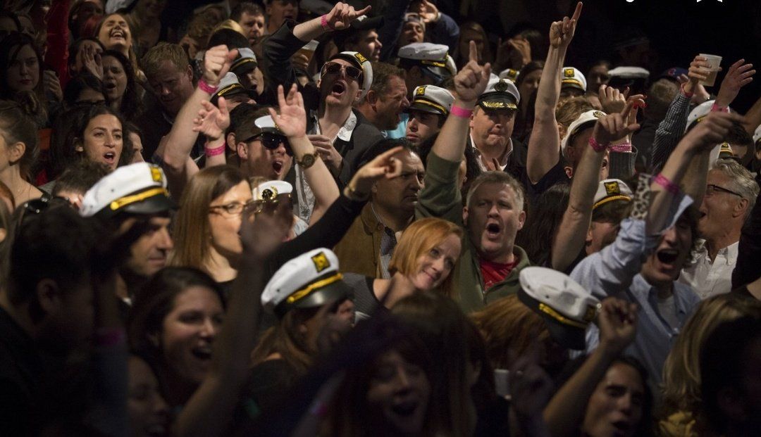 A crowd of people wearing captain hats are dancing in a dark room.