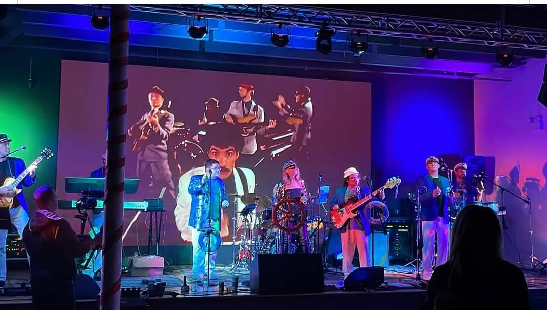 A group of people are playing instruments on a stage in front of a large screen.