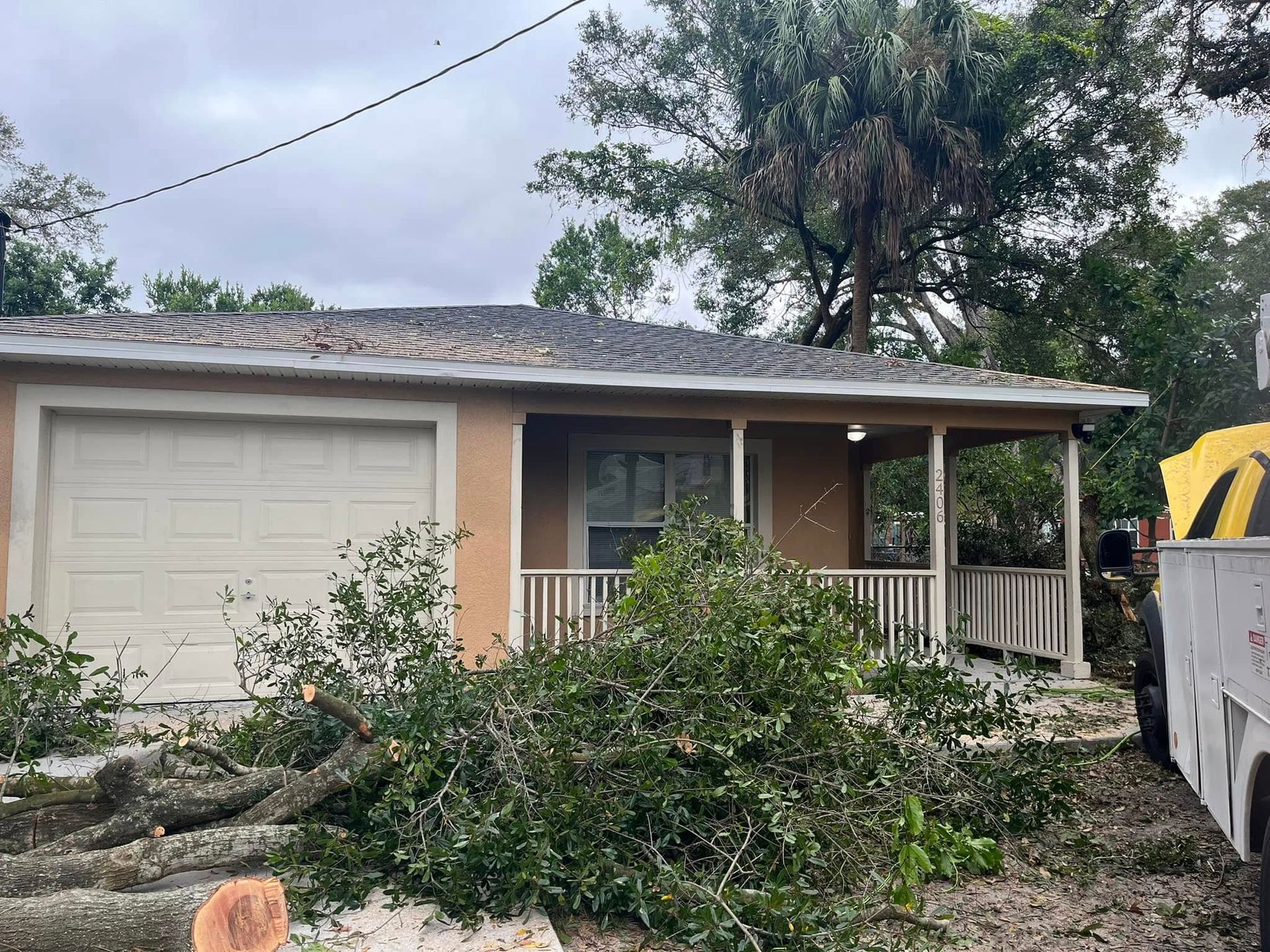 Single-story house with storm damage, fallen tree branches, and a truck in the driveway Emergency Tree Service