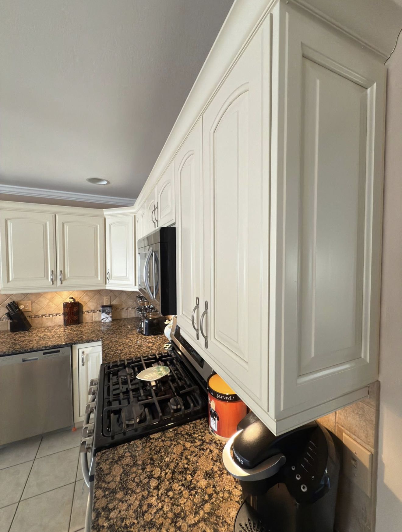 Kitchen with cream-colored cabinets, granite countertops, and a black stovetop and microwave.