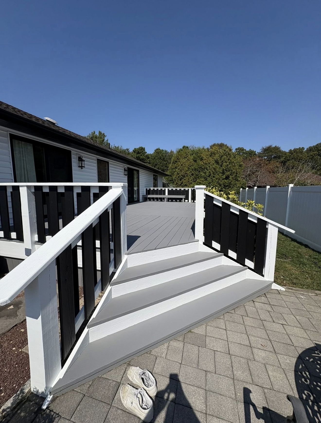 Gray deck with white railing and black accents leading to a house. Sunny day.