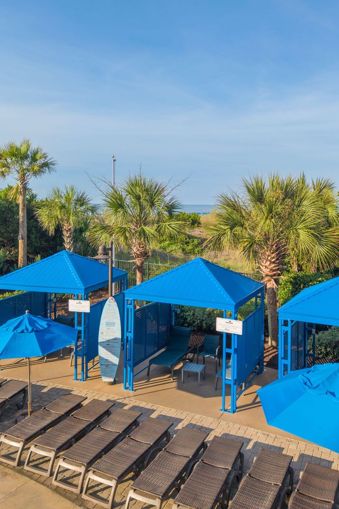 Blue metal benches under a shaded bus stop shelter with a paved walkway and greenery beyond