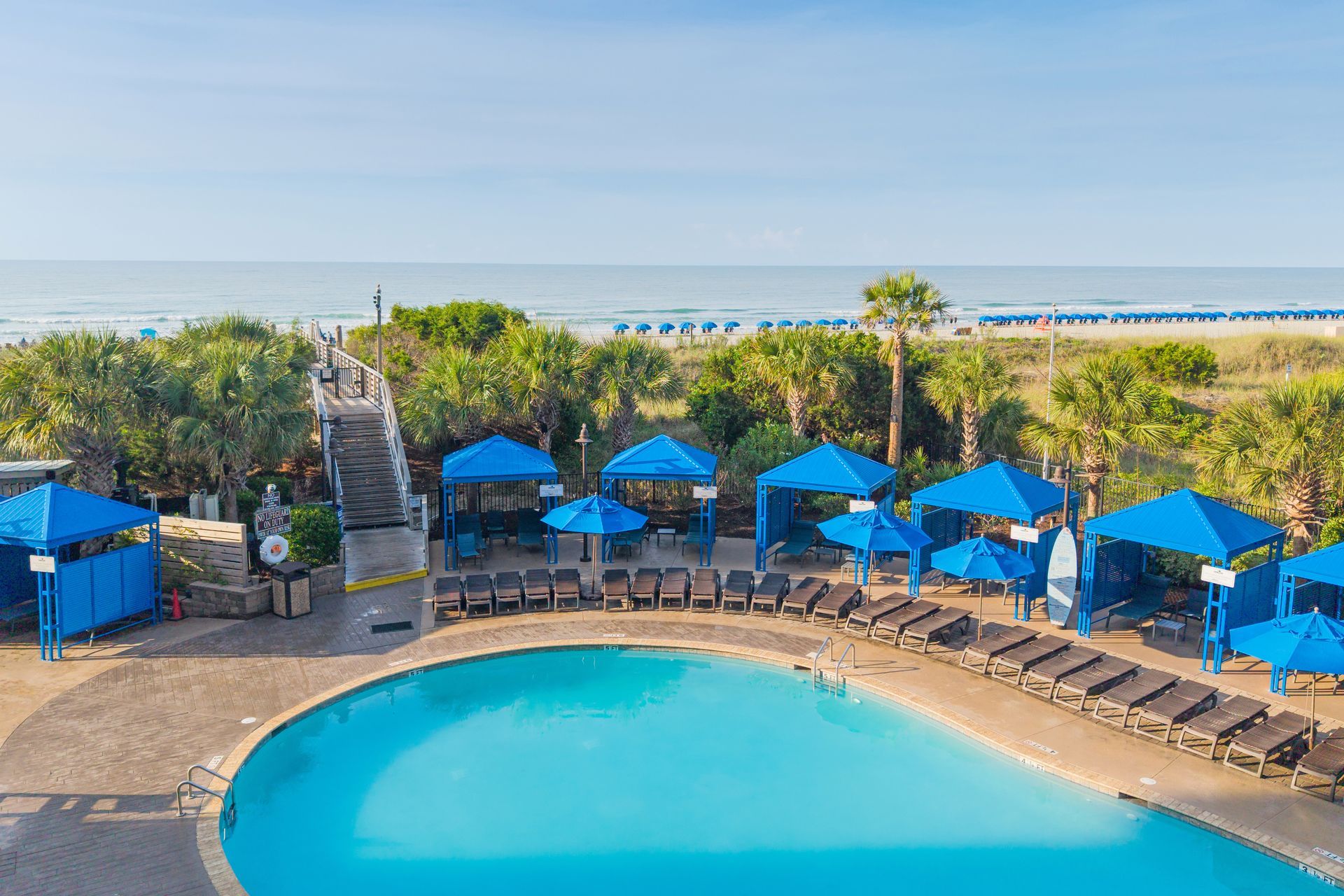 Blue poolside cabanas and lounge chairs beside a turquoise swimming pool under cloudy skies