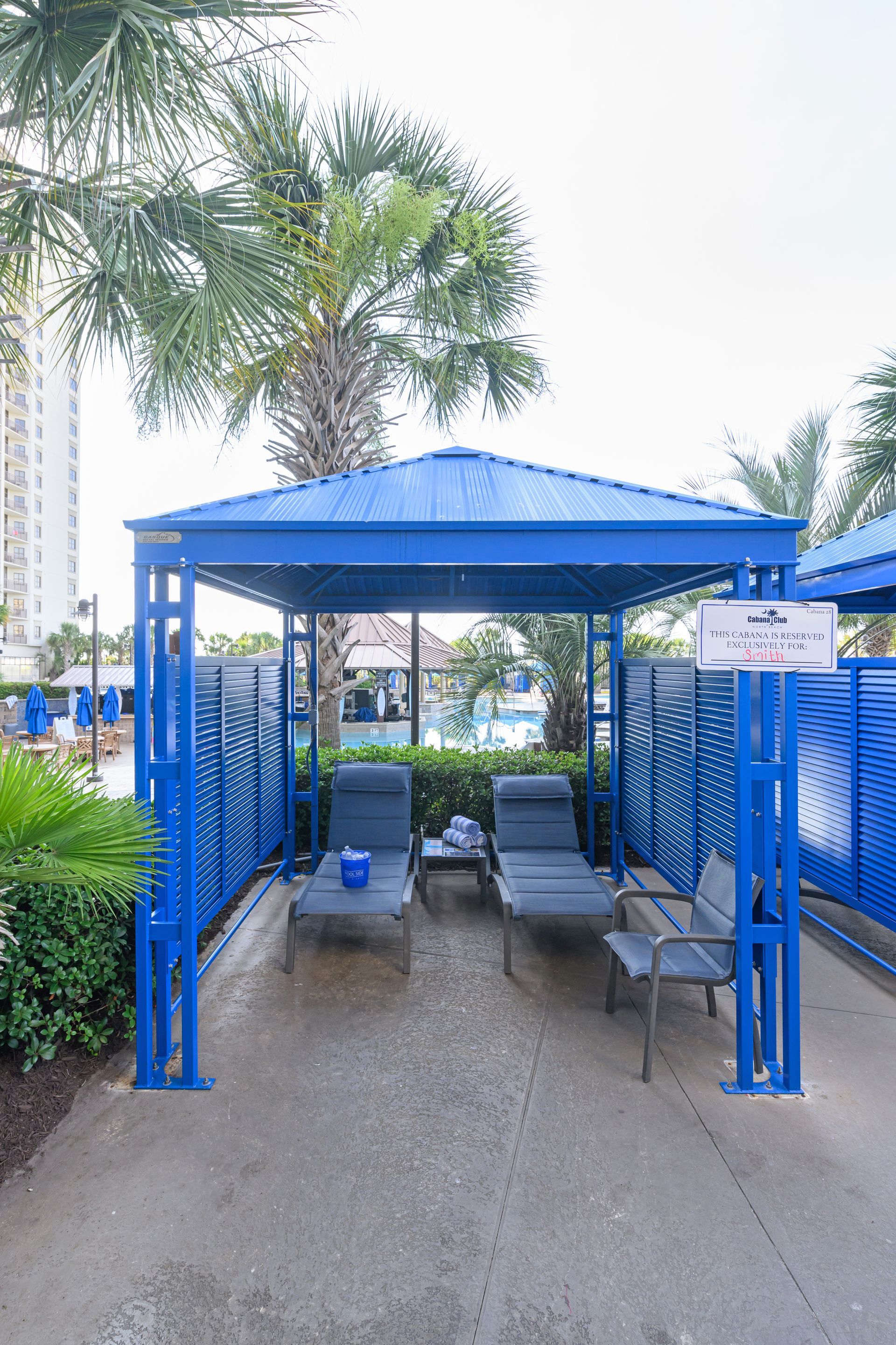Blue shaded lounge chairs and a small table under a metal canopy on a patio area