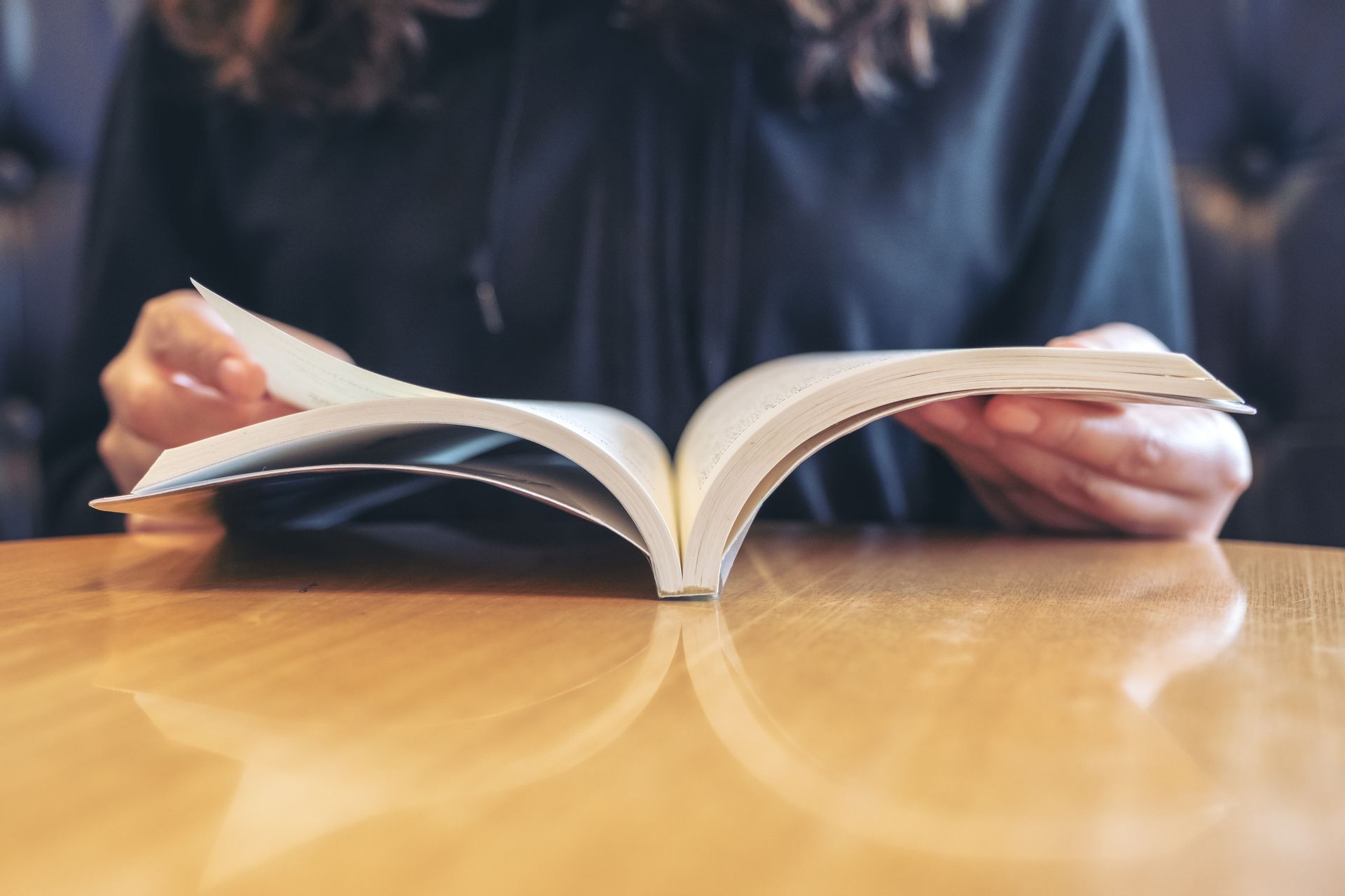 A woman is sitting at a table reading a book.