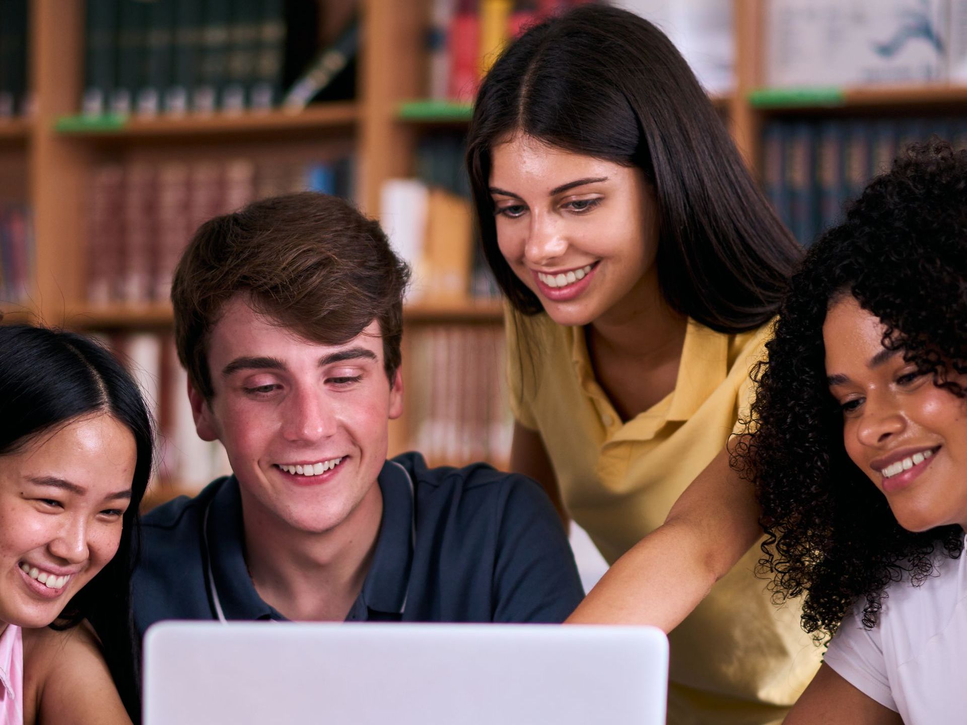 A group of young people are looking at a laptop computer in a library.