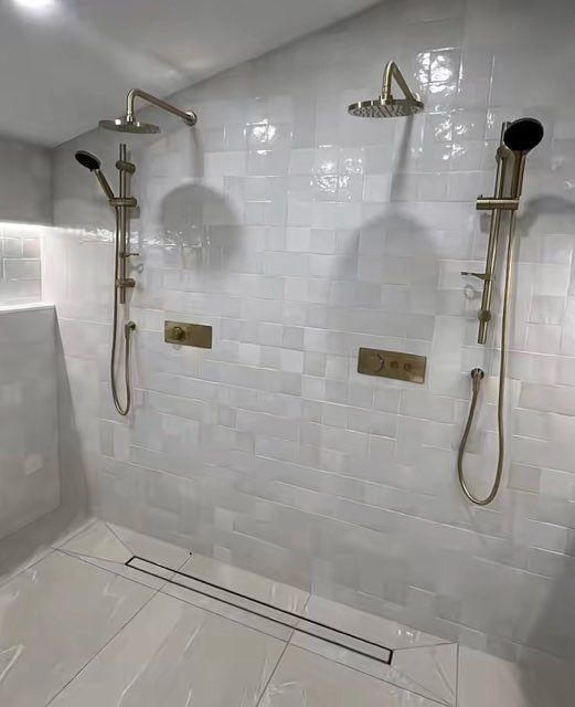Il y a deux douches dans la salle de bain avec du carrelage blanc.