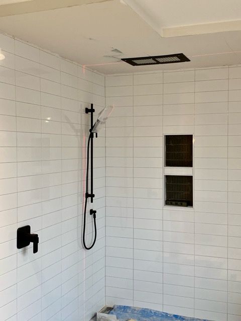 Une salle de bain avec du carrelage blanc et une pomme de douche noire