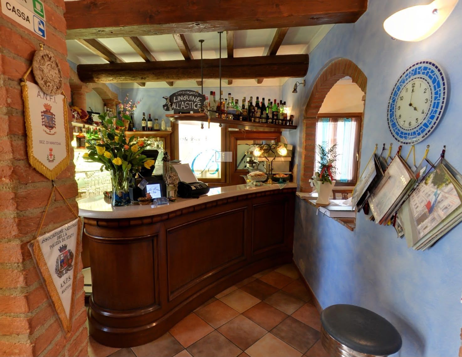 Accogliente bancone di un caffè con fiori, menu appesi, pavimento in terracotta e travi in legno rustico