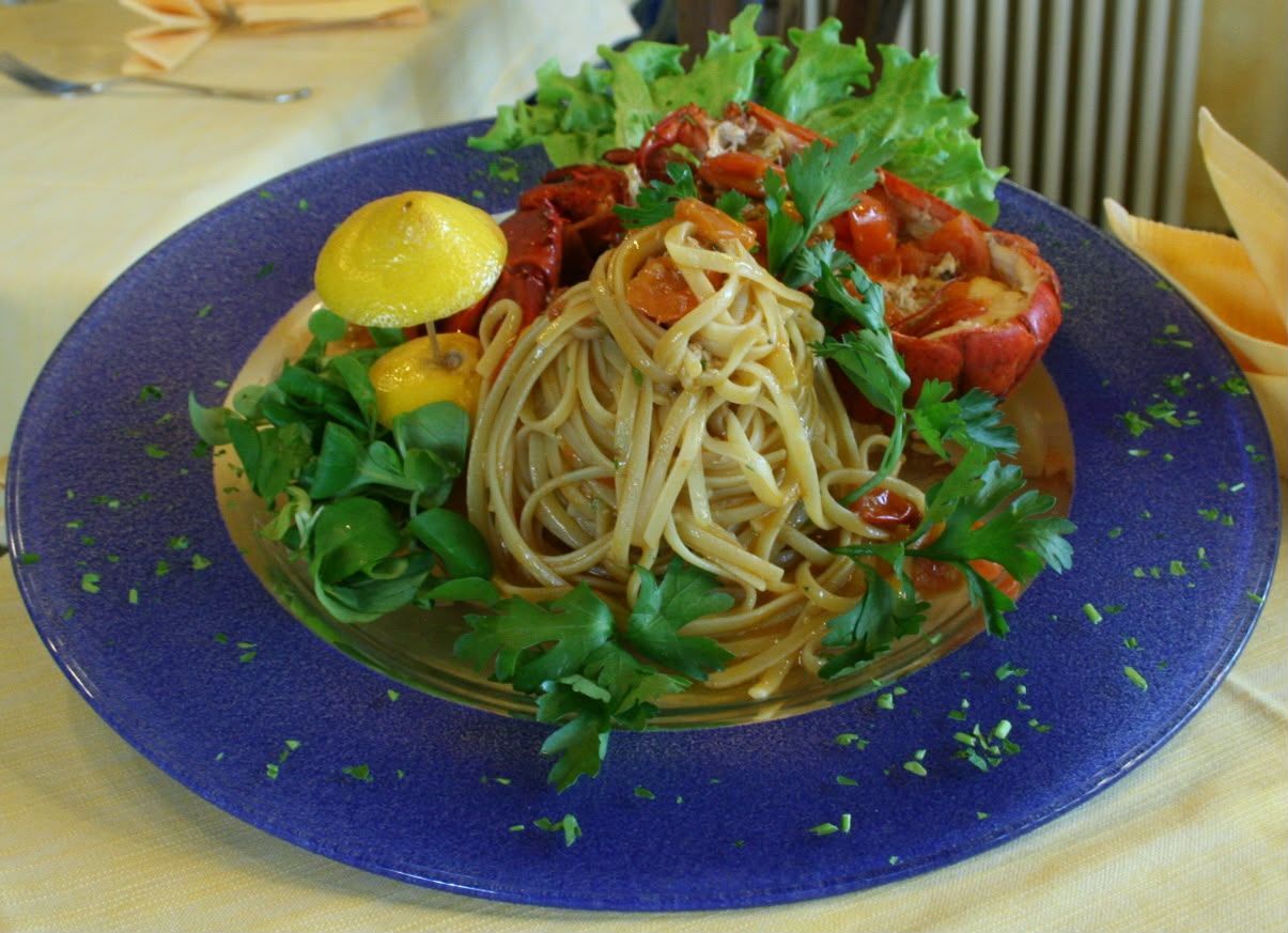 Piatto di spaghetti con pomodori, verdure e uno spicchio di limone su un piatto blu