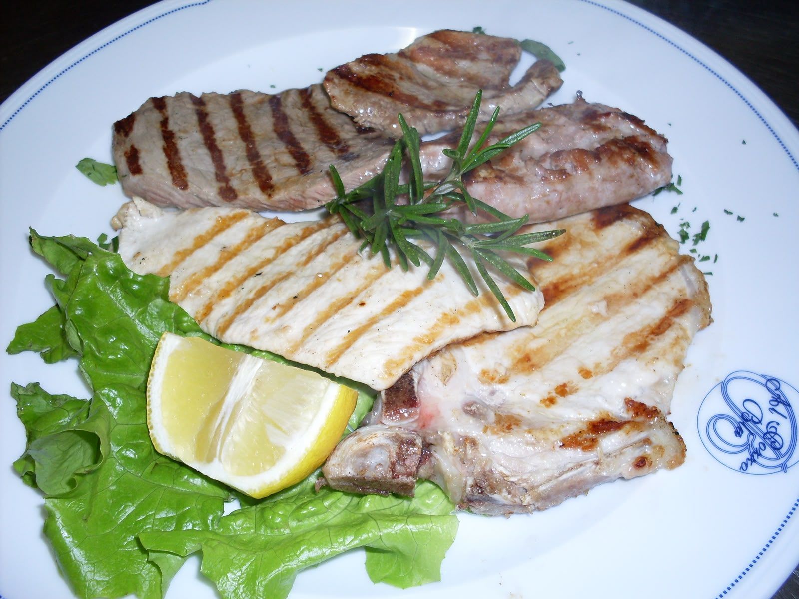 Filetti di pesce alla griglia con spicchio di limone e rosmarino su un piatto bianco, guarniti con lattuga