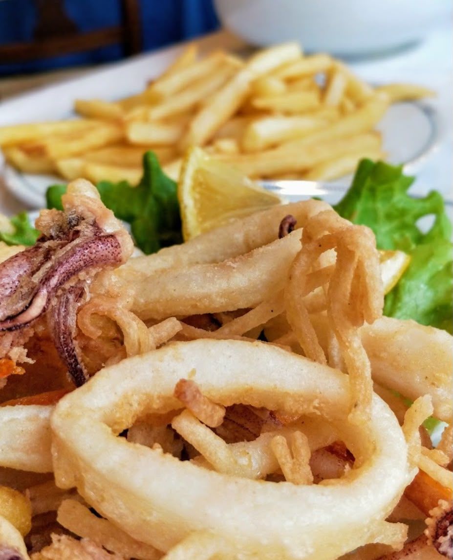 Anelli di calamari fritti e patatine serviti su un piatto con lattuga e spicchi di limone
