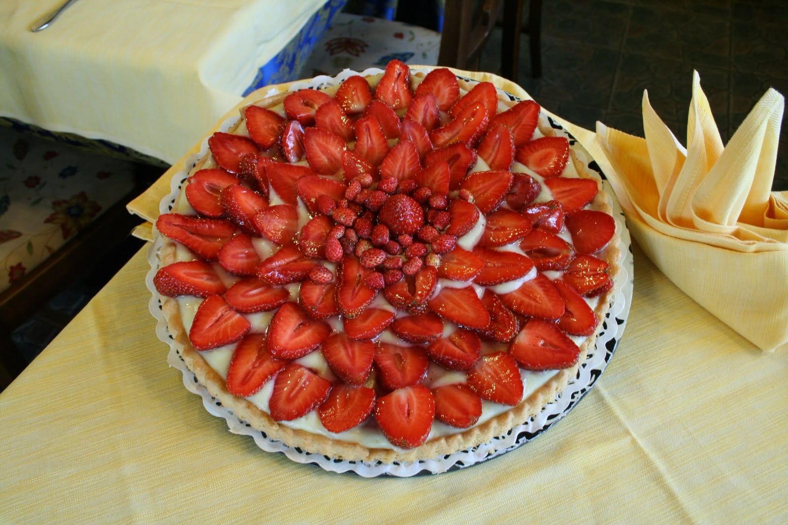 Crostata alle fragole su un vassoio, guarnita con fragole a fette, accanto a una tazza piena di tovaglioli piegati