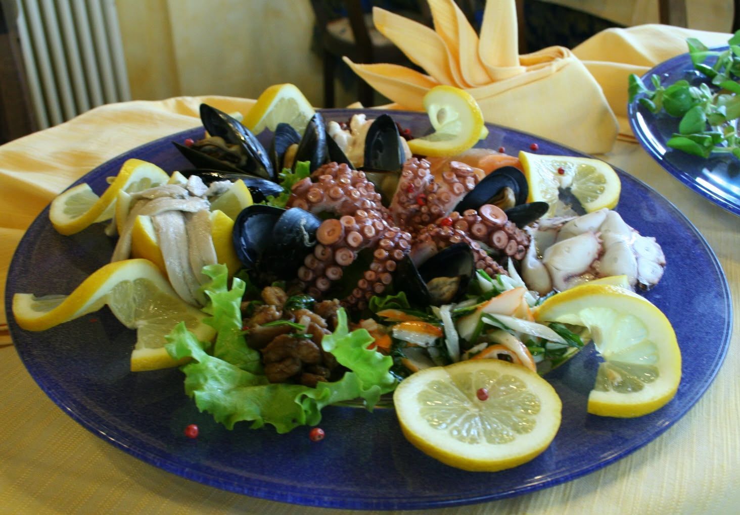 Piatto di frutti di mare con cozze, fette di limone, olive e verdure su un piatto blu