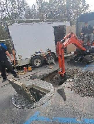 a man is standing next to a manhole cover next to a small excavator .