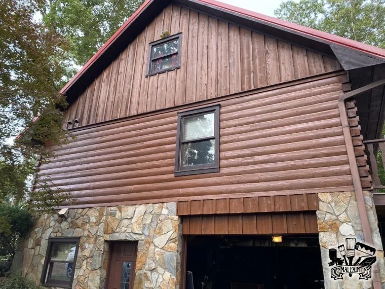 Log cabin-style house with stone and wood siding, garage opening, and a small upper window
