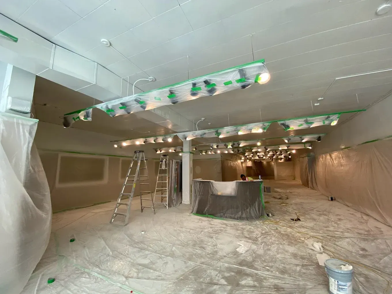 Painted room under renovation with plastic-covered walls, ladders, and ceiling lights being installed