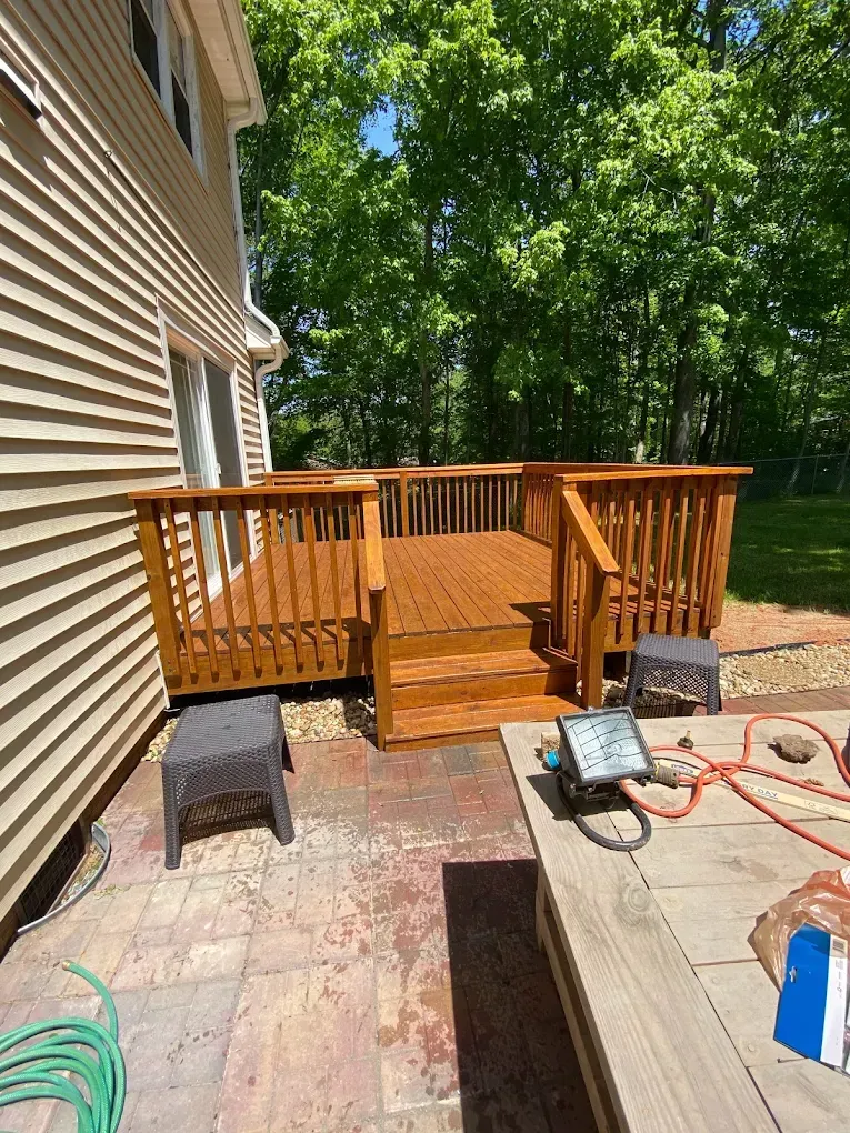Wooden backyard deck attached to a house, with steps, railing, and tools on a patio during construction.