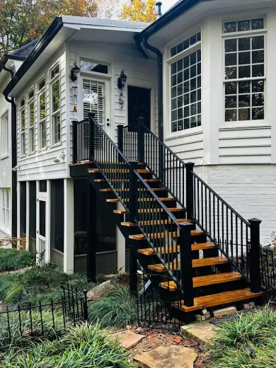 White house exterior with black staircase and railings leading to a front porch, surrounded by greenery