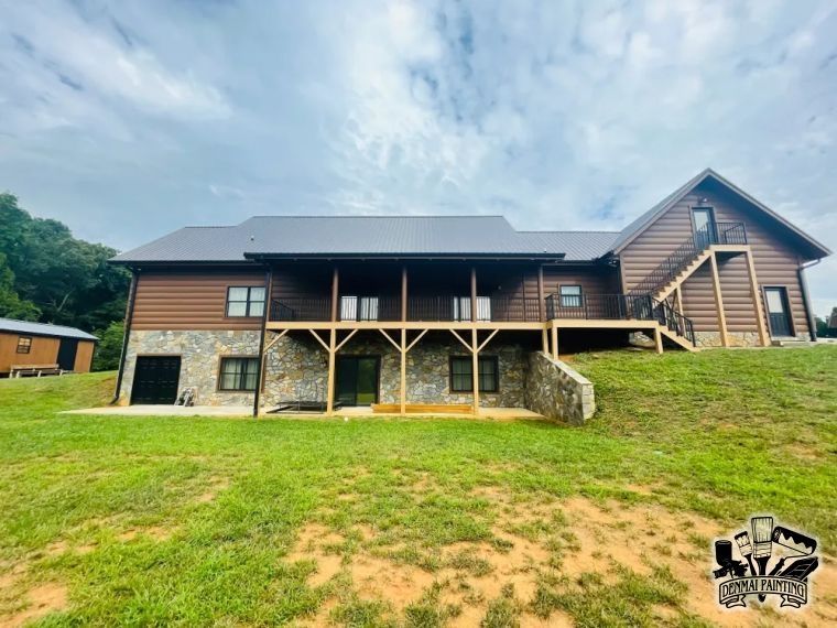 Rustic lodge-style house with stone pillars, wood siding, and a grassy front yard under a cloudy sky