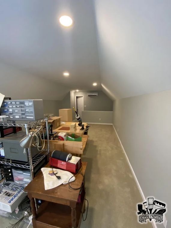 Attic storage room with boxes, shelves, and a work table under sloped white ceiling and lights
