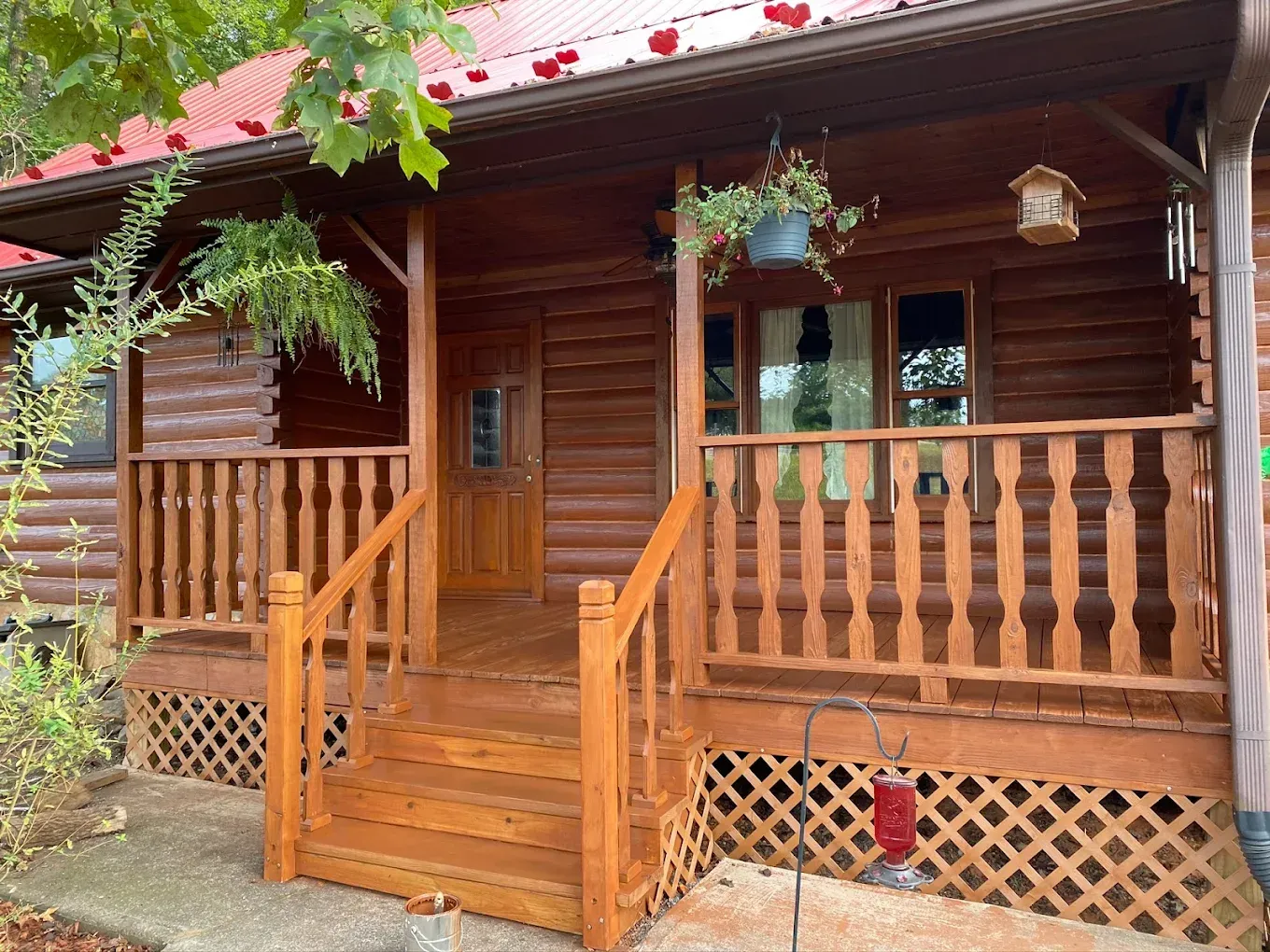 Wooden front porch with steps, railing, hanging flowers, and a screened door on a cabin-style house.