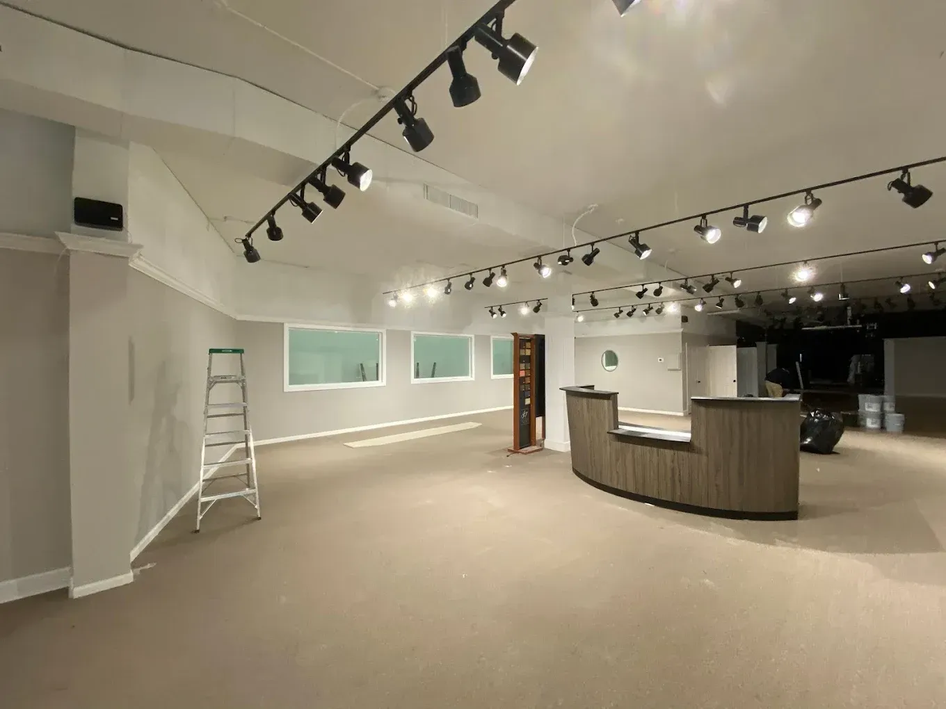 Empty retail showroom with beige carpet, track lighting, curved counter, and ladder against the wall