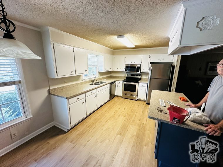 Bright kitchen with white cabinets, wood floor, stainless stove, and a person at the island holding a red cloth.
