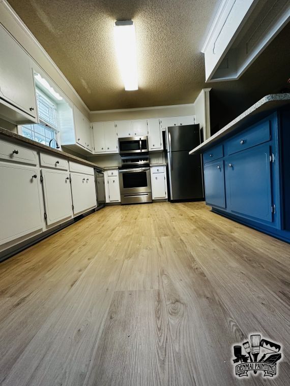 Wide-angle view of a bright kitchen with white cabinets, black appliances, and a blue island cabinet