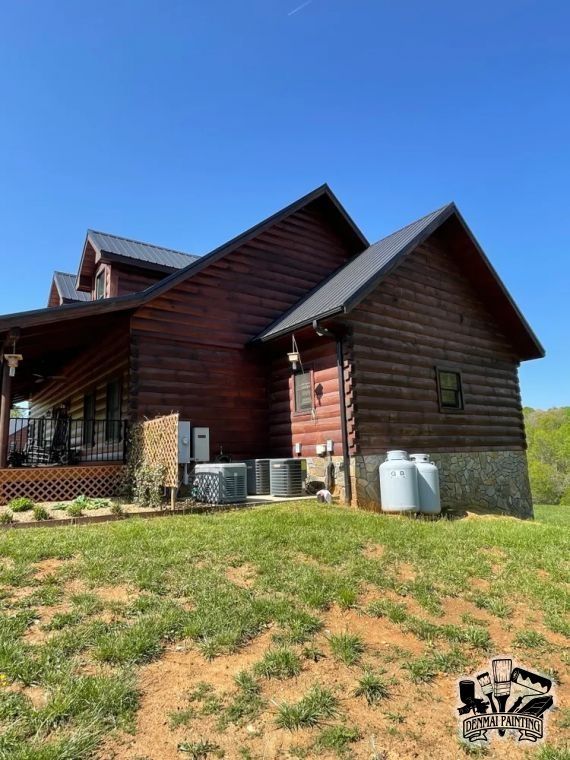 Rustic red wooden cabin with gray roof, air conditioners, and grassy yard under a clear blue sky