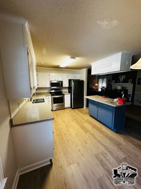 Modern kitchen with white cabinets, black appliances, blue island, and light wood flooring