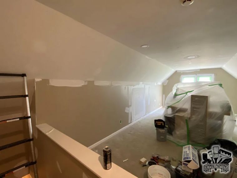 Room under renovation with masked window, ladder, paint supplies, and beige walls being painted