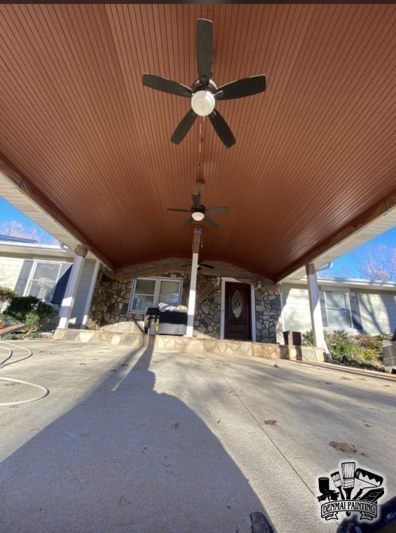 Covered porch with brown ceiling, ceiling fans, and driveway view toward a house entrance.