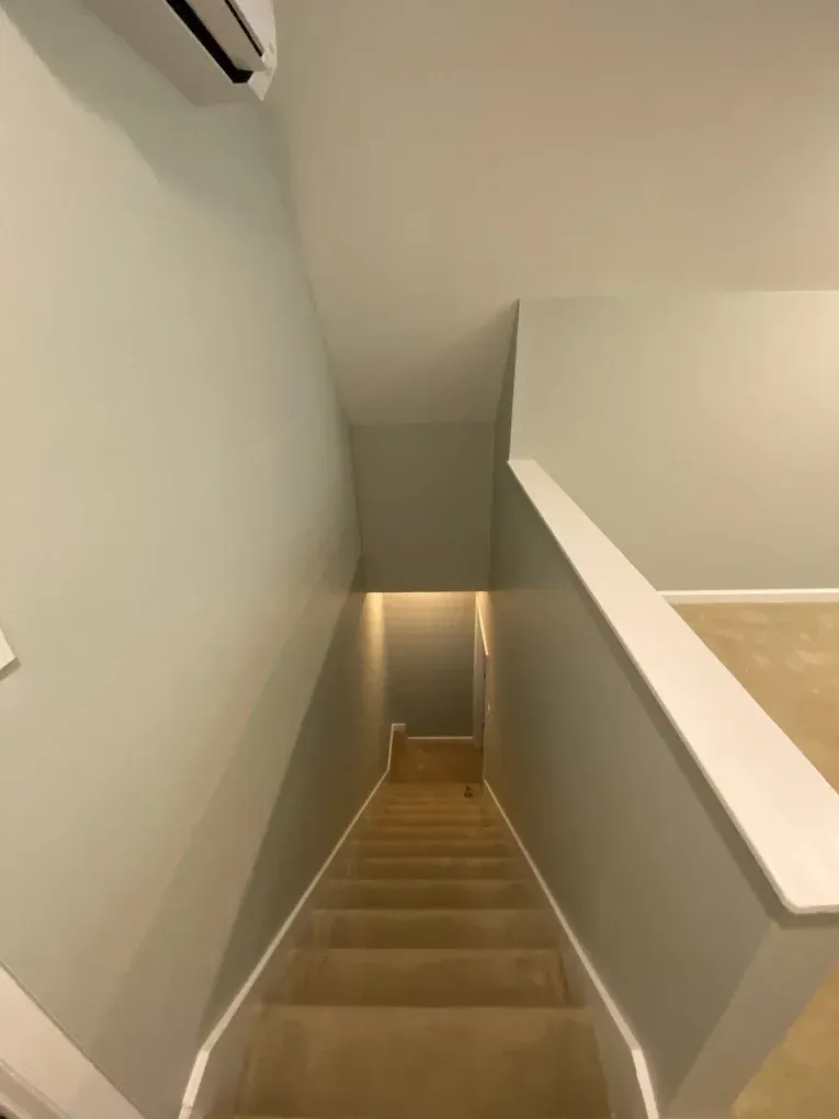 Staircase descending to a lower level with white walls and a beige handrail.
