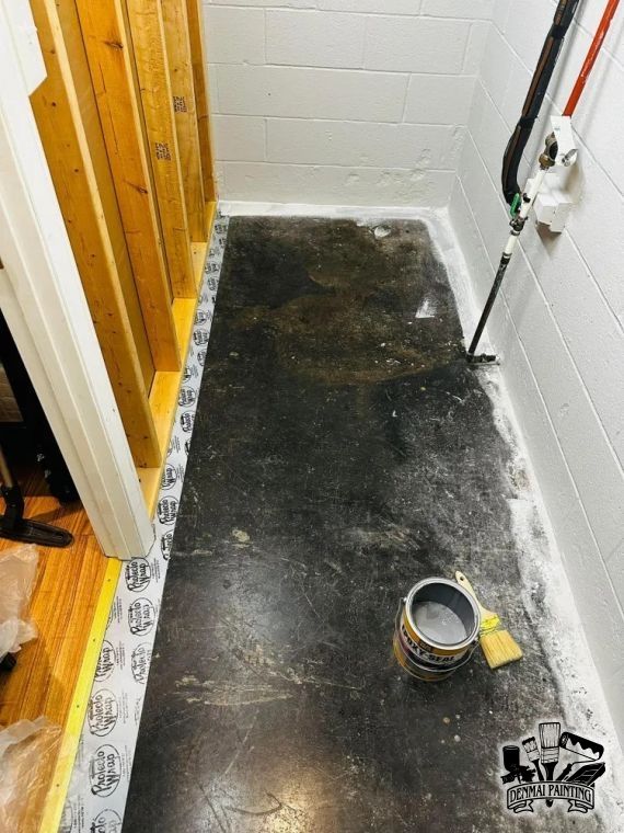Narrow hallway floor with fresh black flooring, a paint can, and a brush beside white walls.