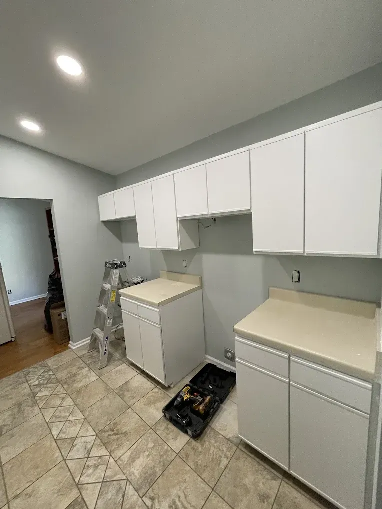 Bright laundry room with white cabinets, washer, beige countertops, and tiled floor under ceiling lights