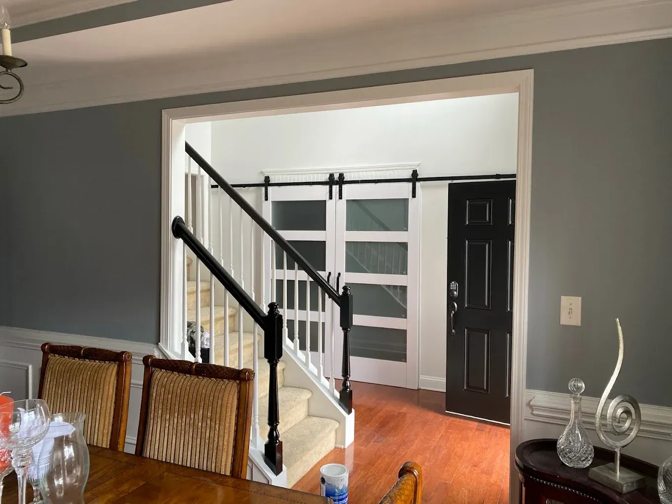 Dining room opening to a hallway with a staircase and dark front door, gray walls, and hardwood floors