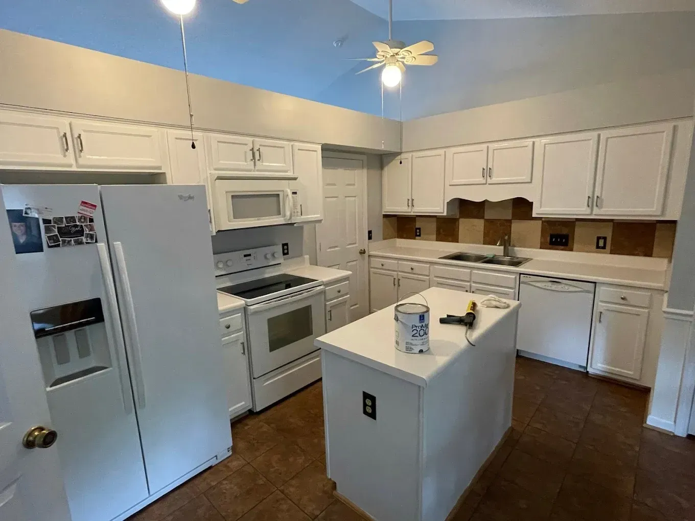 Bright white kitchen with stainless appliances, center island, and blue ceiling.