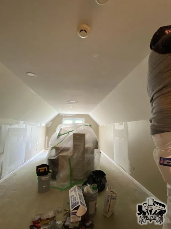 Hallway under renovation, with plastic-covered furniture, paint supplies, and masked walls and ceiling.