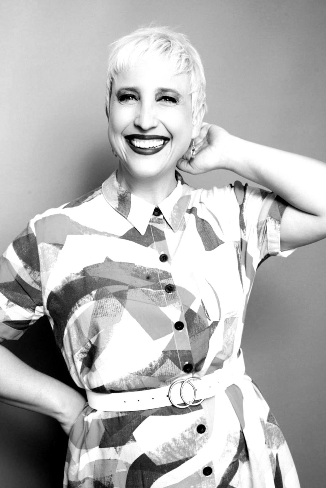 A woman with long hair and hoop earrings is smiling in a black and white photo.