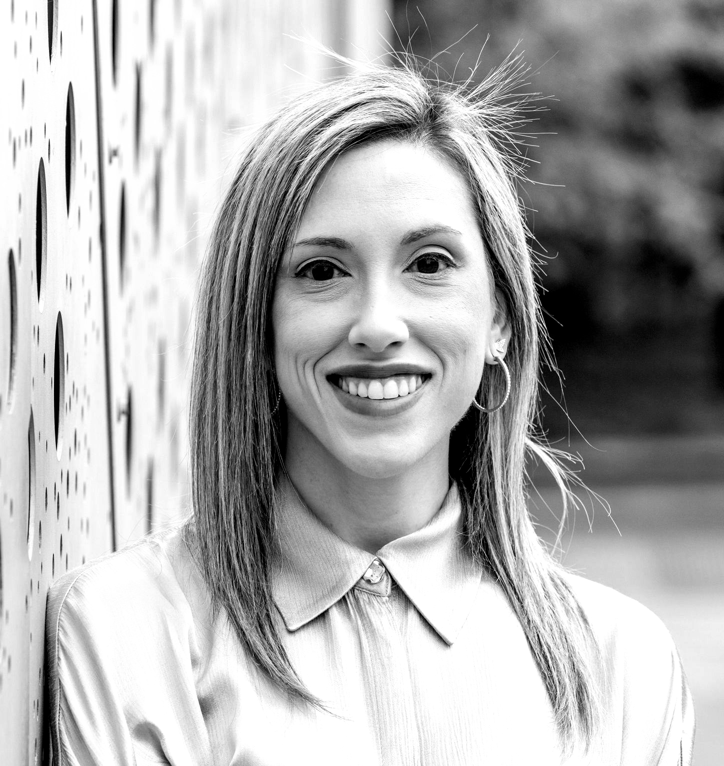 A woman with long hair and hoop earrings is smiling in a black and white photo.