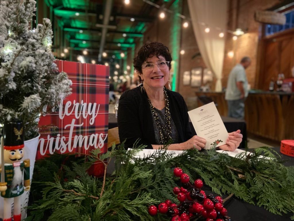 A woman sitting at a festive table holding a menu card for wine tasting and food pairing at Kirchhoff wines