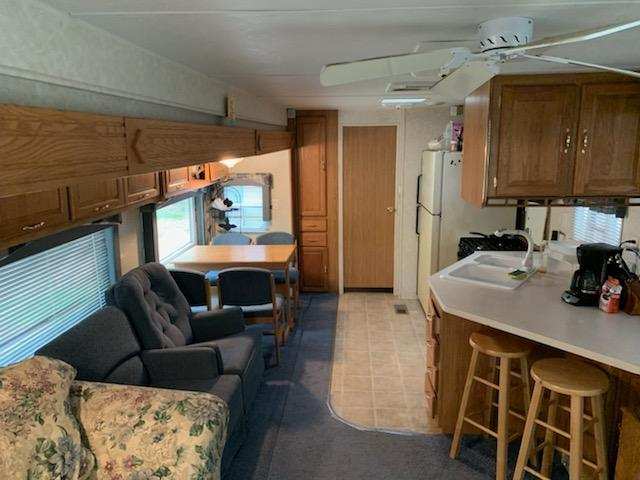 RV interior with sofa, recliners, wood cabinets, and kitchenette area